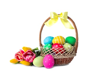 Wicker basket with bright painted Easter eggs and spring flowers on white background