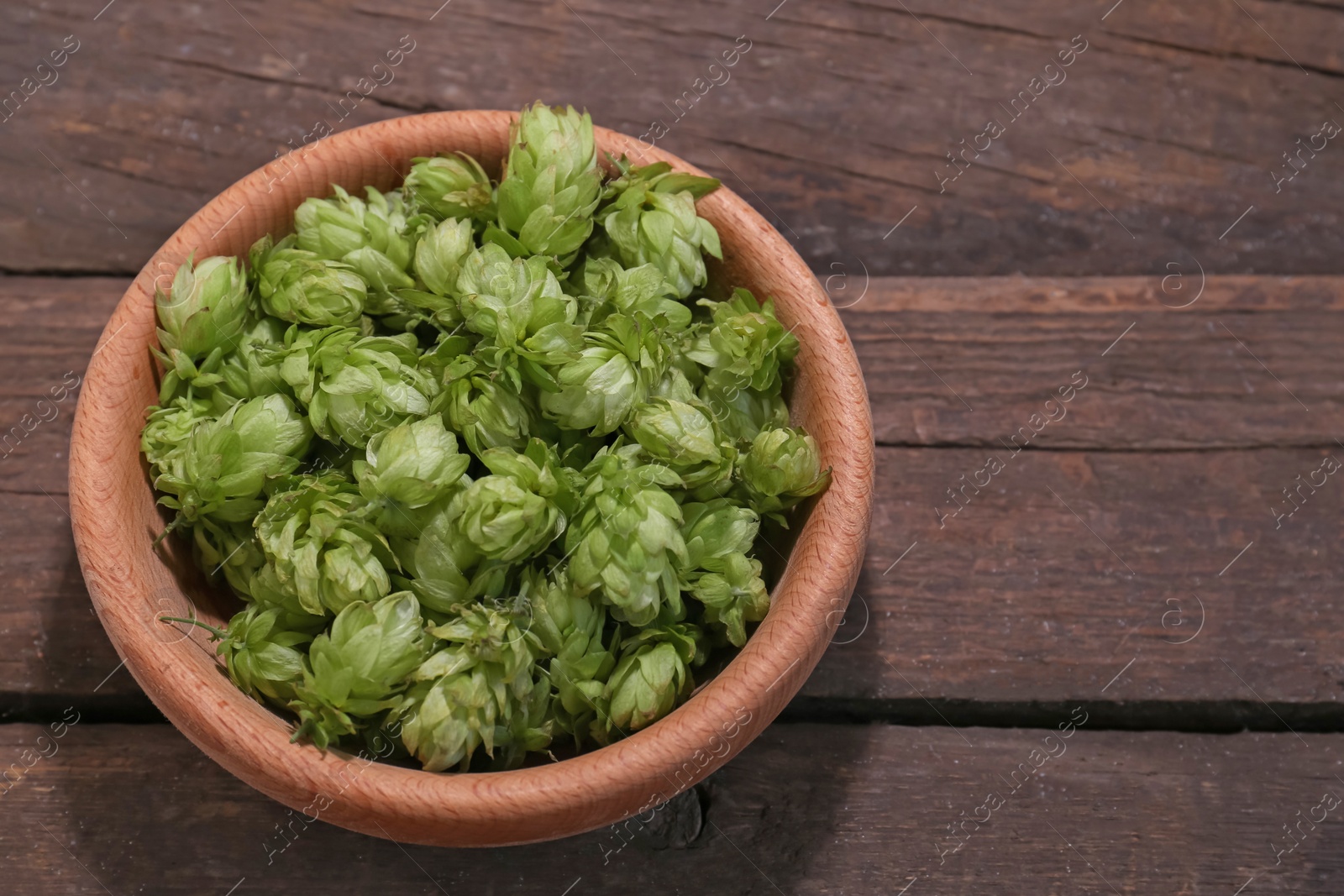 Photo of Bowl of fresh green hops on wooden table, above view. Space for text