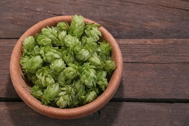 Bowl of fresh green hops on wooden table, above view. Space for text