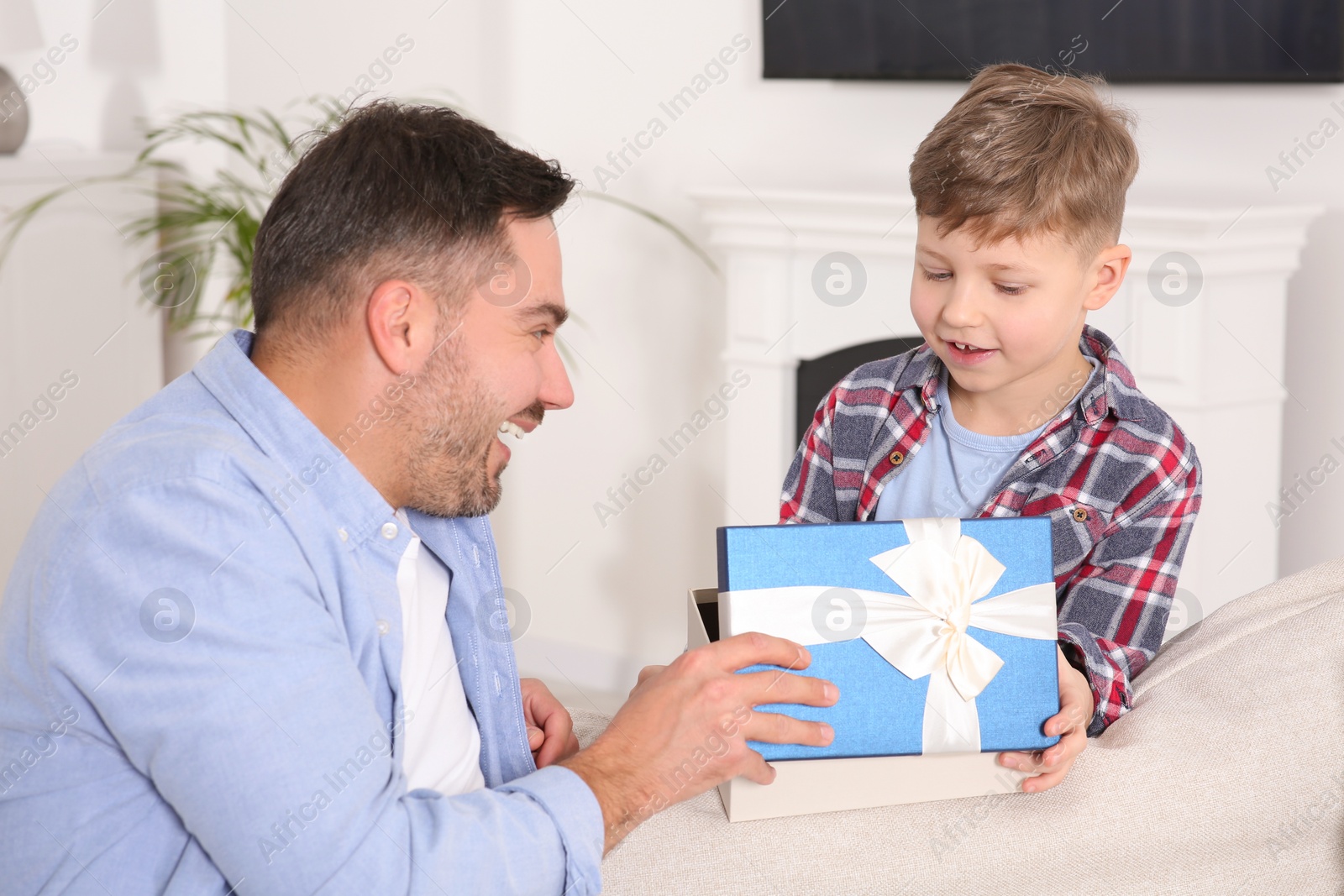 Photo of Cute little boy presenting his father with gift on sofa at home