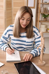 Photo of Woman drawing in sketchbook with pen at wooden table indoors