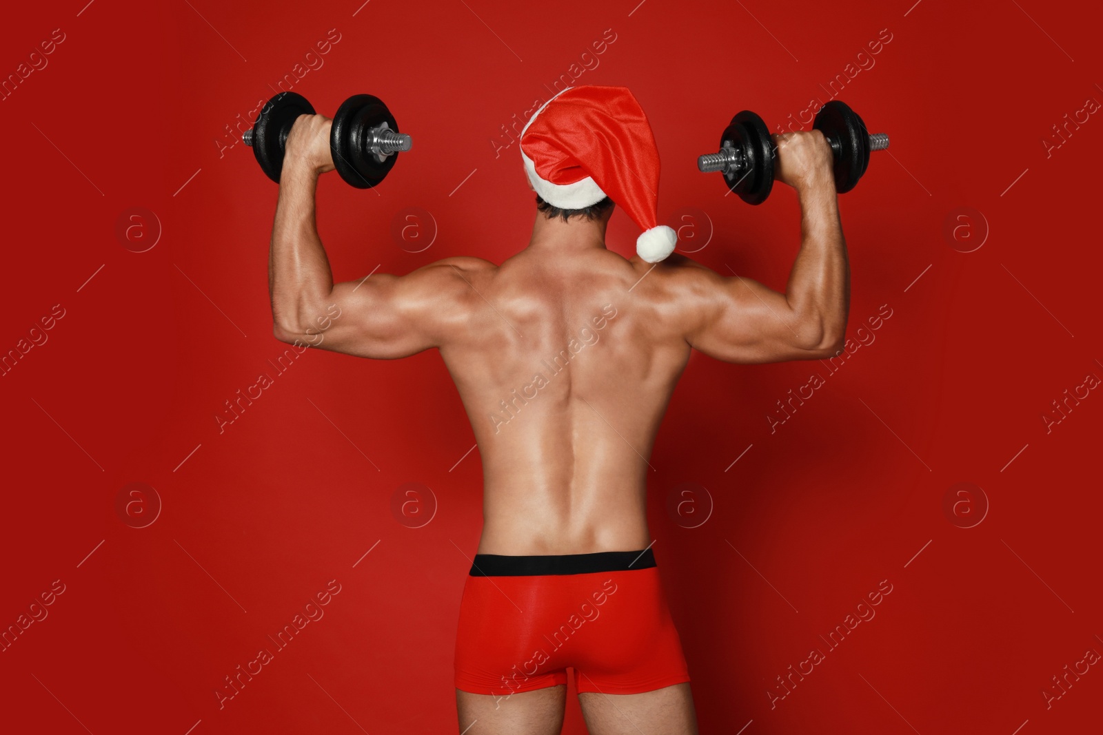 Photo of Sexy shirtless Santa Claus with dumbbells on red background