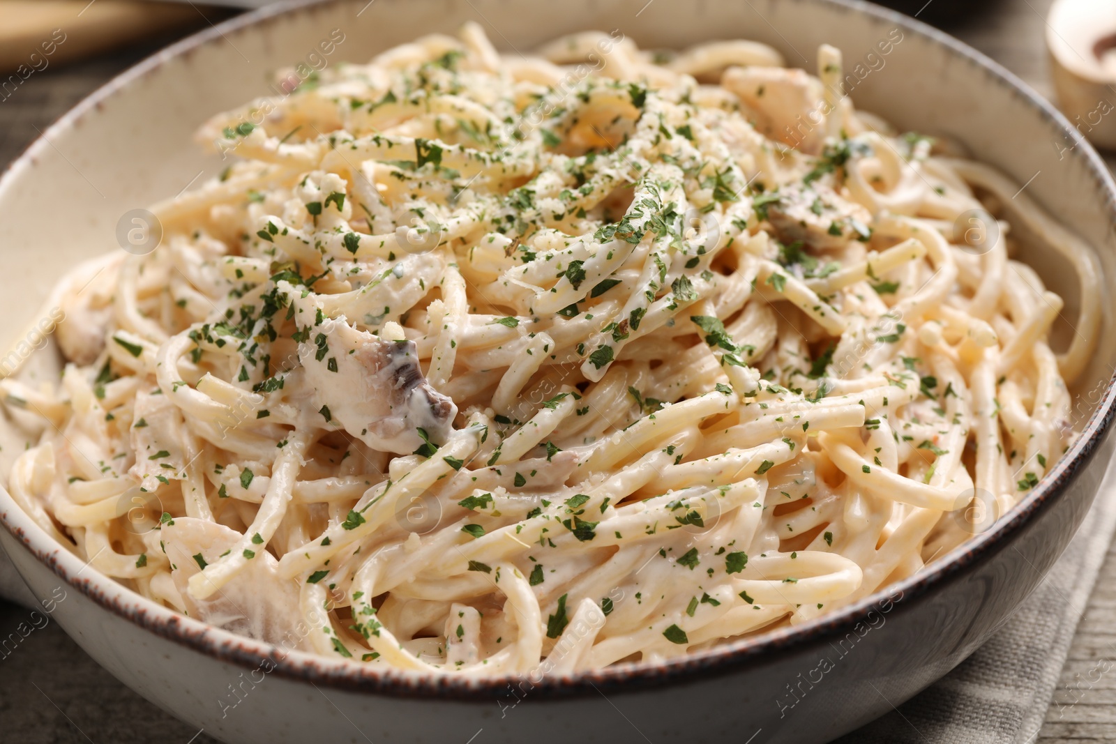 Photo of Bowl of delicious pasta with mushroom sauce and parsley on wooden table, closeup