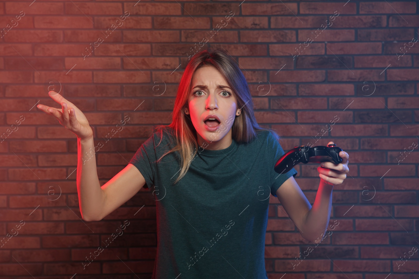 Photo of Emotional young woman playing video games with controller near brick wall