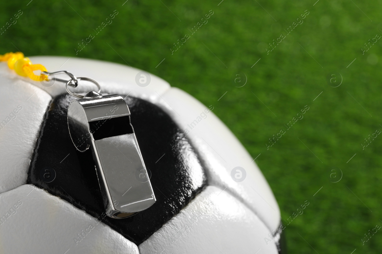 Photo of Football referee equipment. Soccer ball and metal whistle on green grass, closeup with space for text