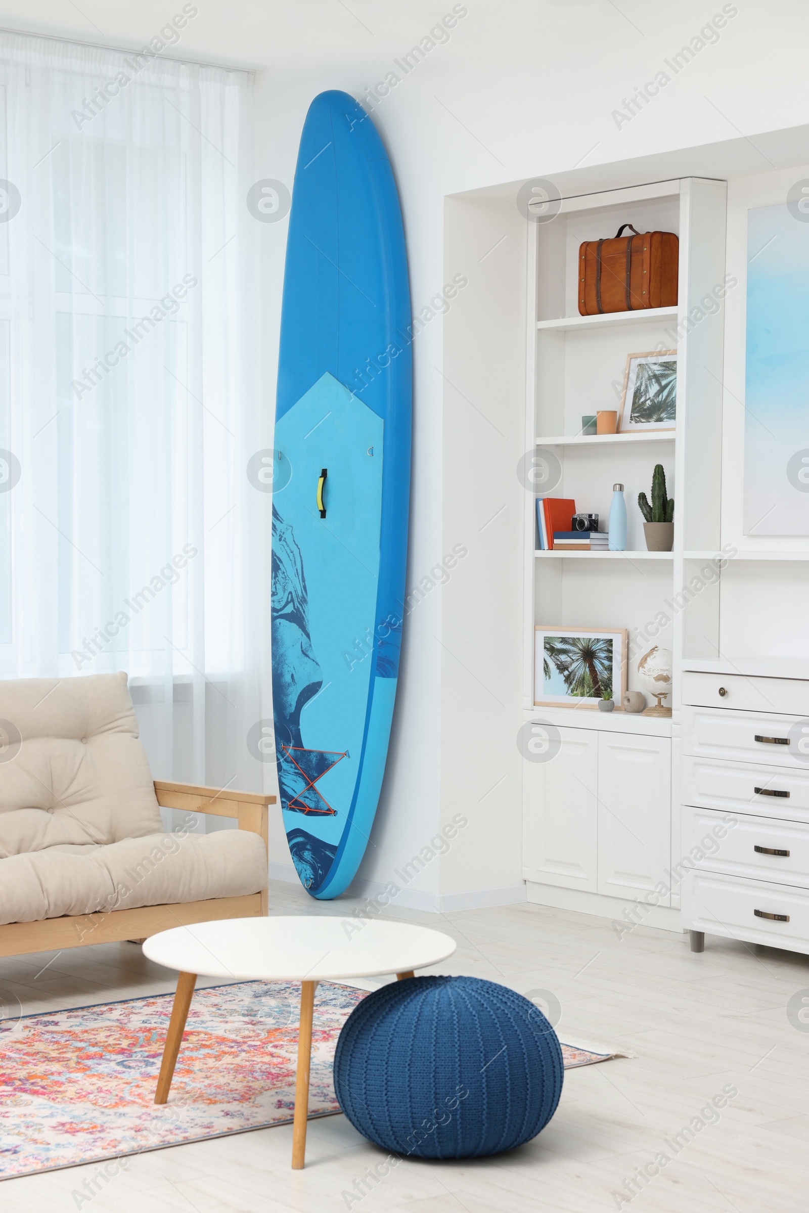 Photo of SUP board and modern furniture in stylish living room. Interior design