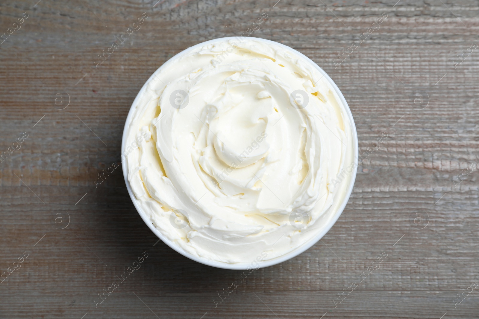 Photo of Bowl of tasty cream cheese on wooden table, top view