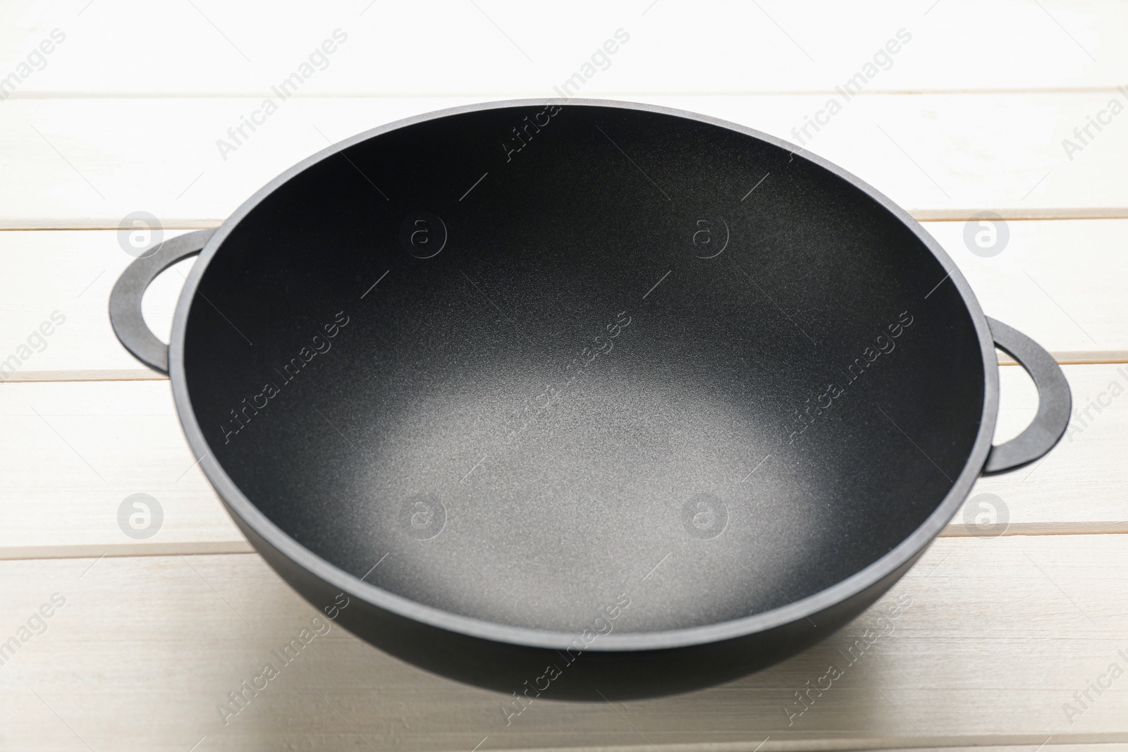 Photo of Empty iron wok on white wooden table. Chinese cookware
