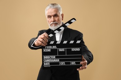 Senior actor holding clapperboard on beige background. Film industry