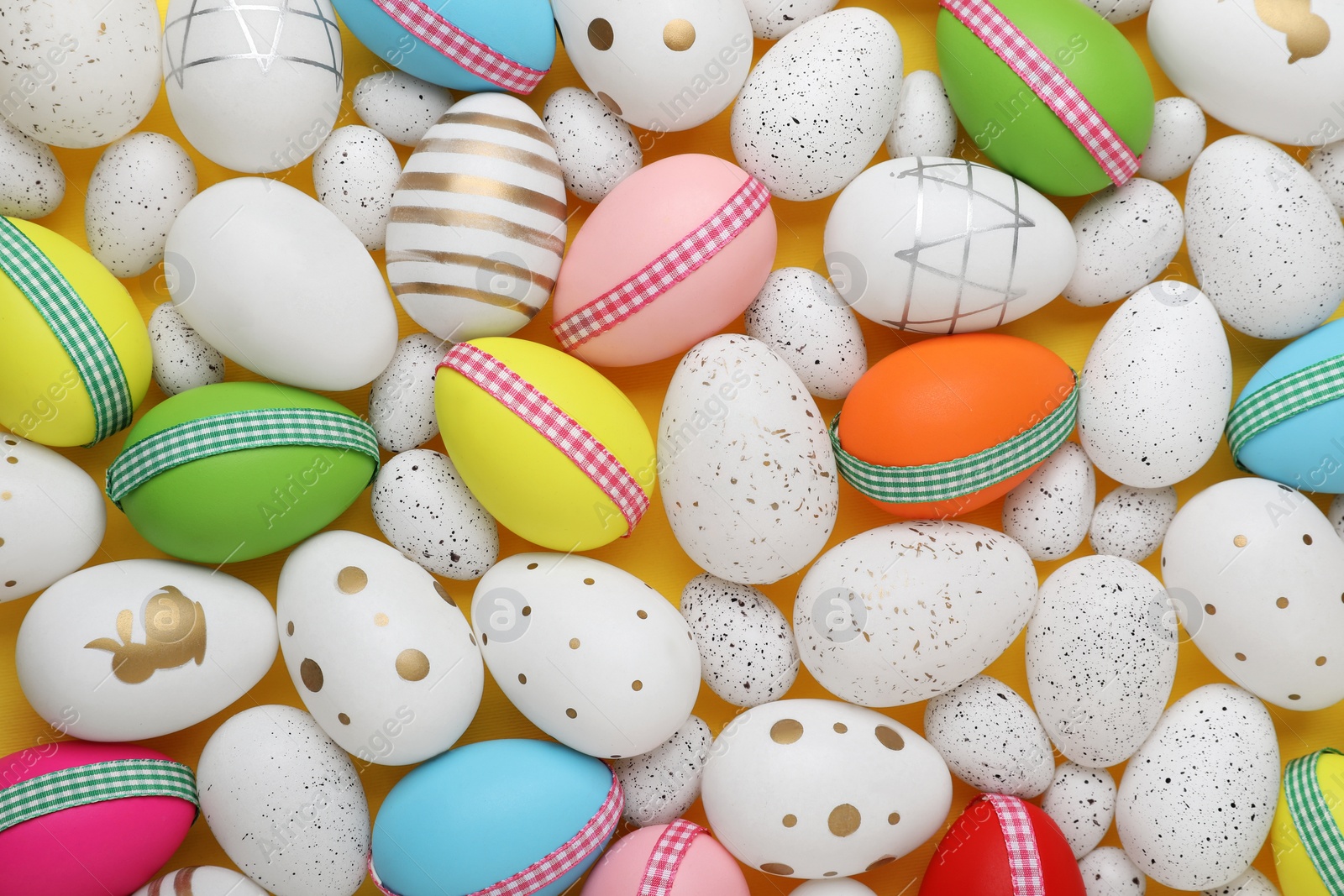 Photo of Festively decorated Easter eggs on yellow background, flat lay