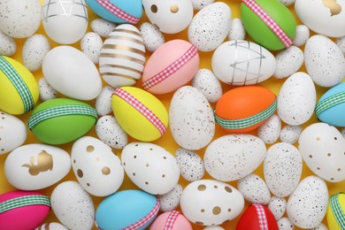 Festively decorated Easter eggs on yellow background, flat lay