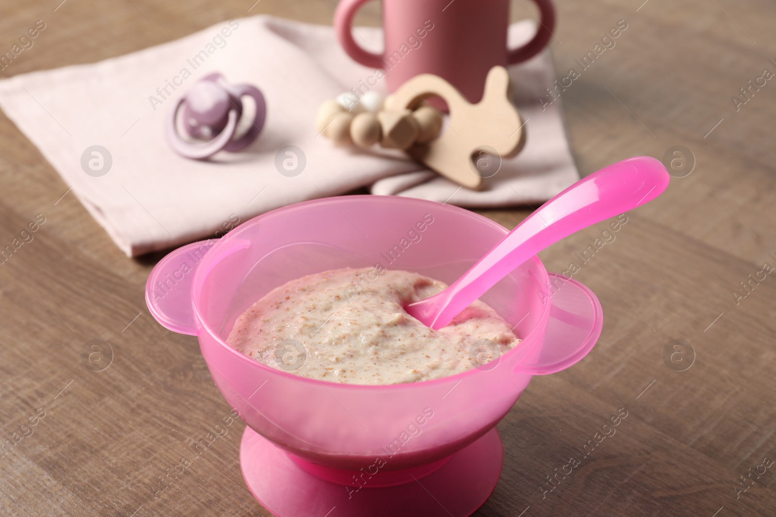 Photo of Baby food. Puree in bowl, drink, toy and soother on wooden table