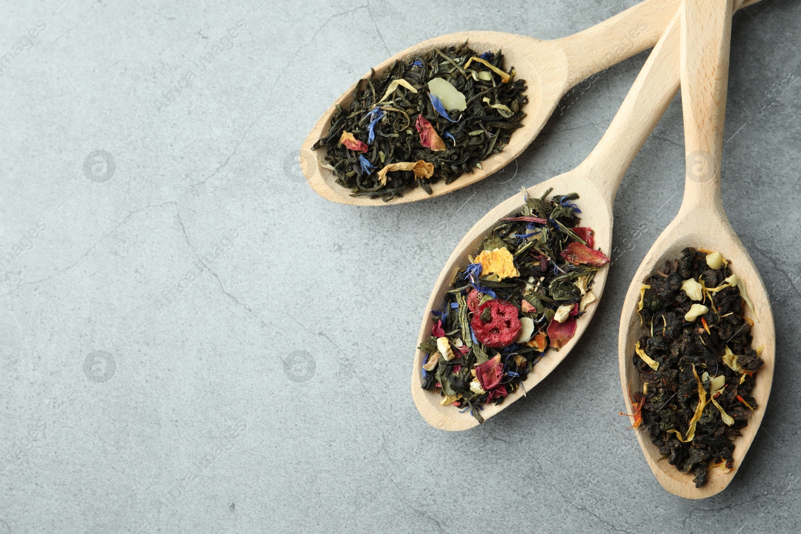 Photo of Different kinds of dry herbal tea in wooden spoons on light grey table, flat lay. Space for text