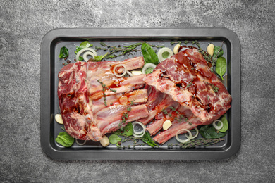 Photo of Raw spare ribs with herbs and seasonings on grey table, top view