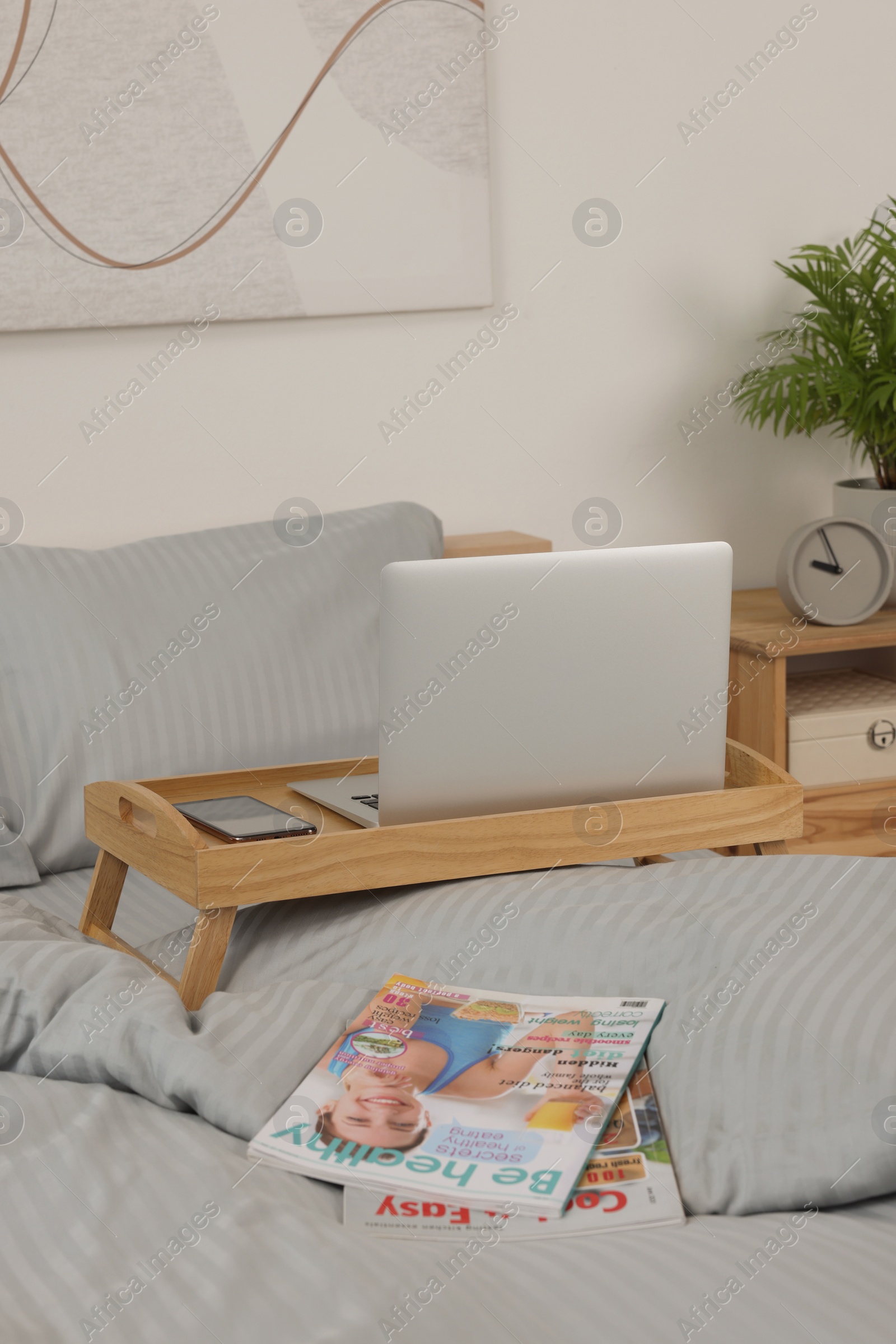 Photo of Wooden tray table with laptop and smartphone on bed indoors