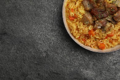 Photo of Delicious pilaf with meat on grey textured table, top view. Space for text
