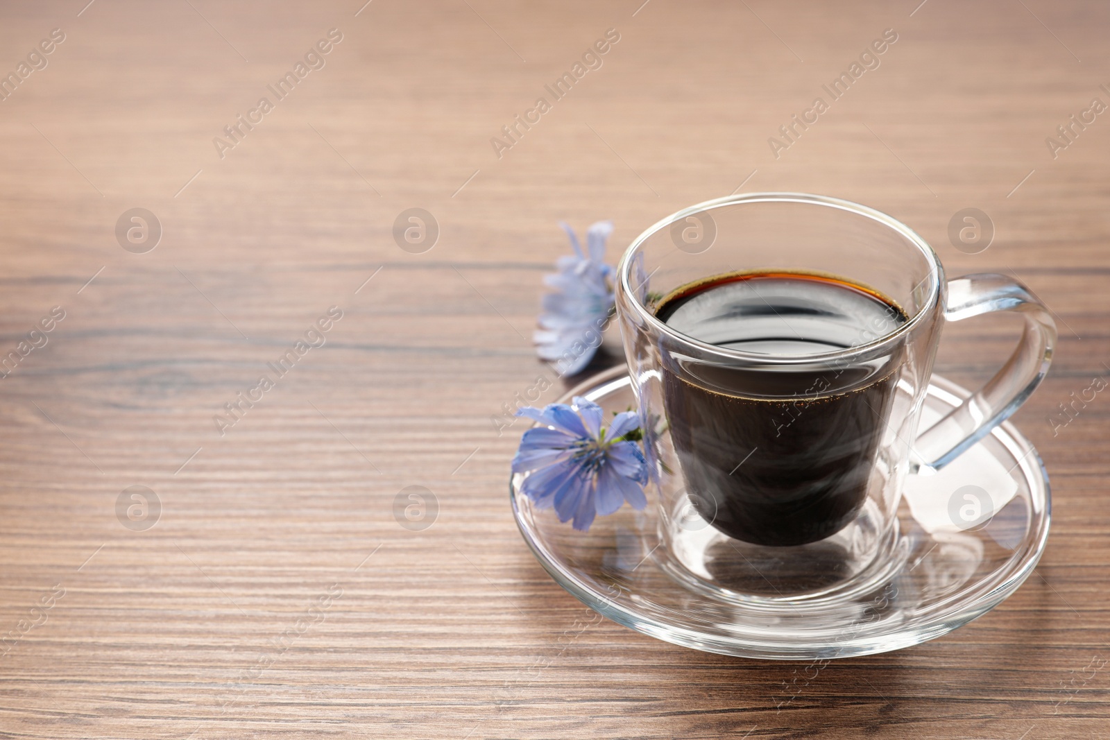 Photo of Glass cup of delicious chicory drink and flowers on wooden table, space for text