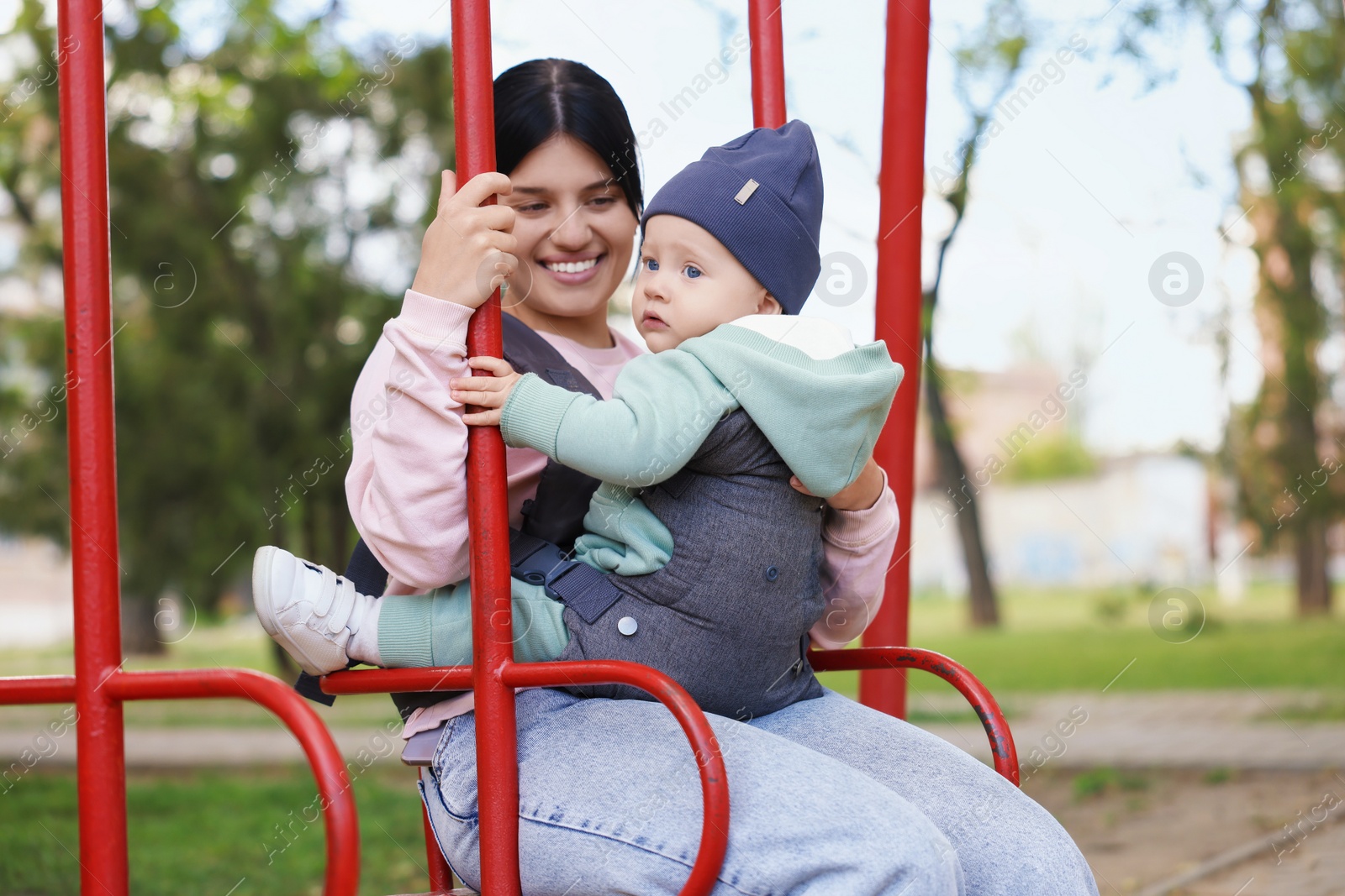 Photo of Mother holding her child in sling (baby carrier) on swing outdoors