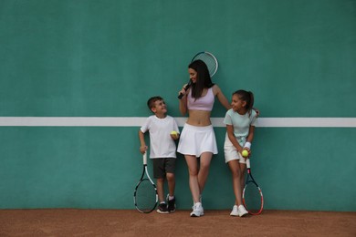 Photo of Young woman with her cute children near green wall on tennis court