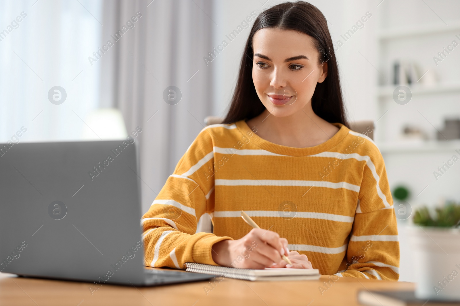 Photo of Young woman watching webinar at table in room