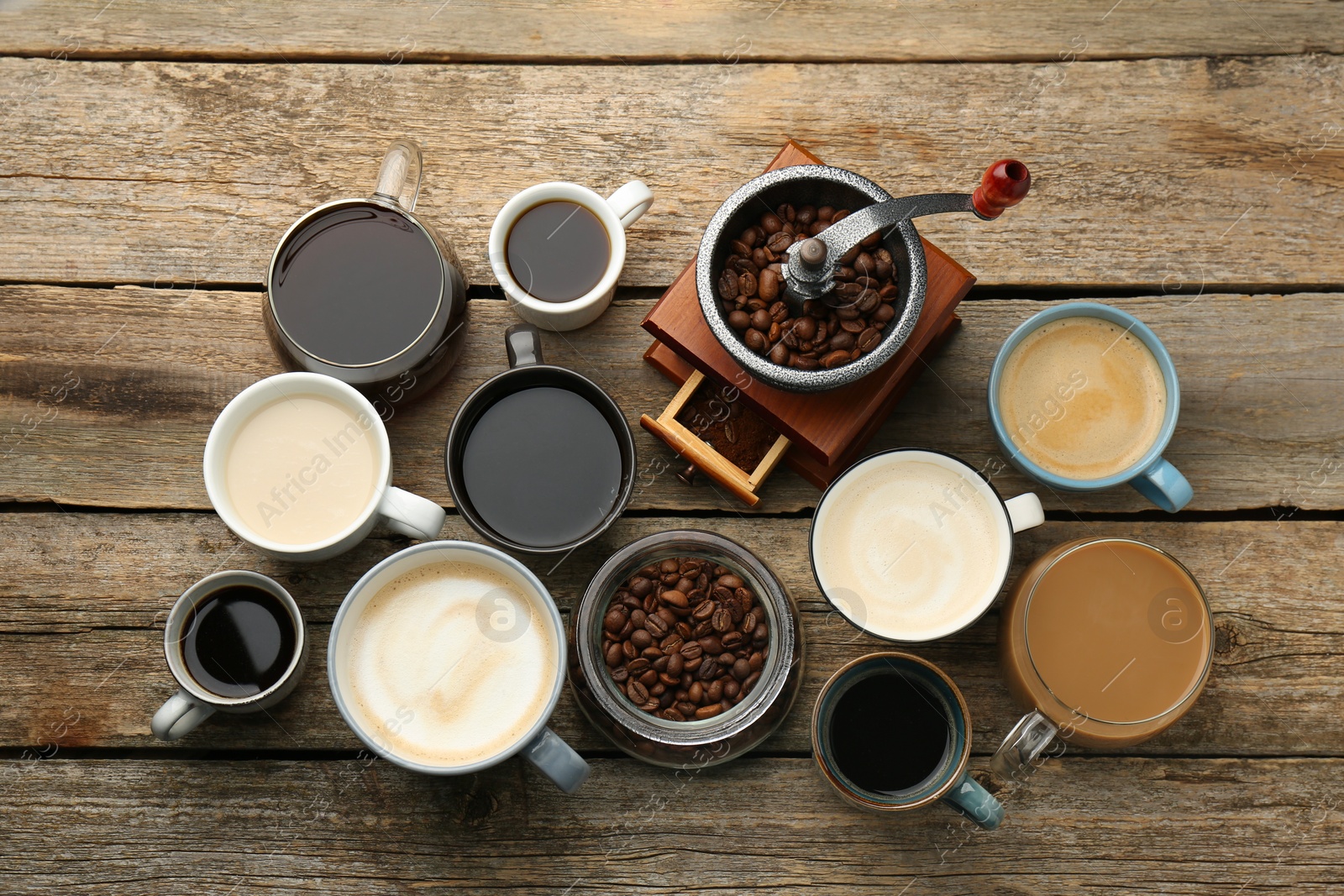 Photo of Different coffee drinks in cups, beans and manual grinder on wooden table, flat lay