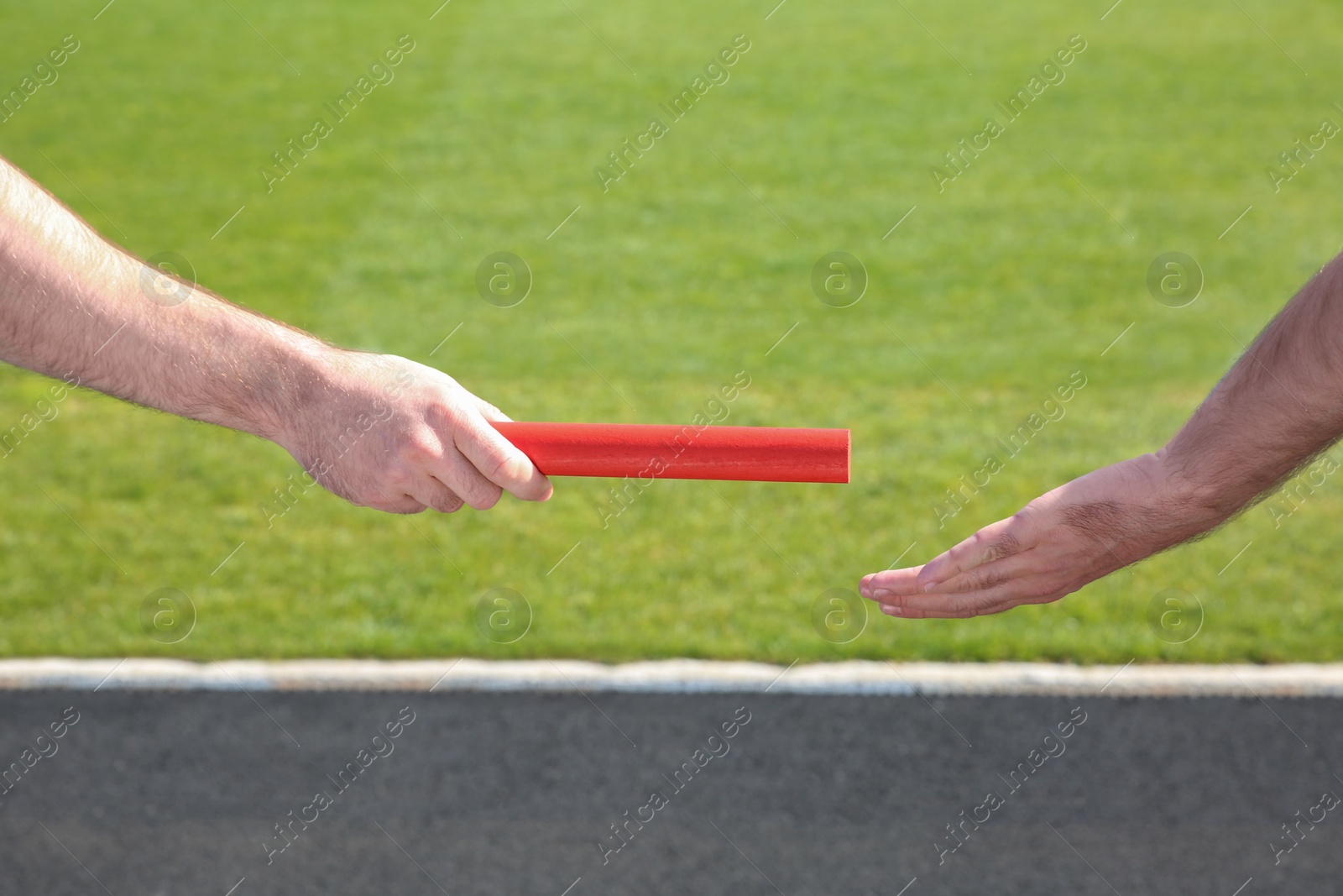 Photo of Man passing baton to his partner at stadium, closeup