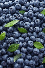 Photo of Wet fresh blueberries with green leaves as background, top view