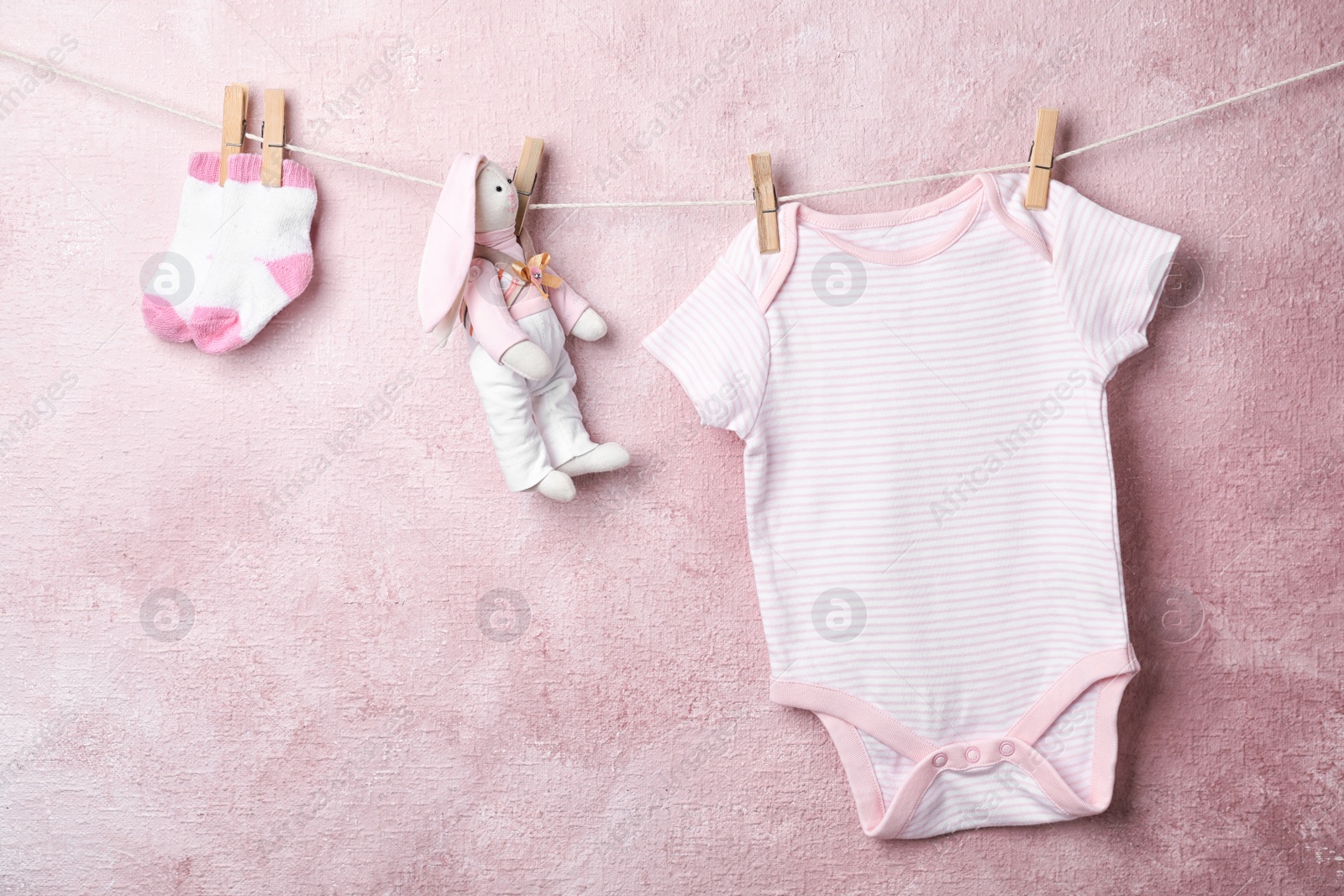 Photo of Baby clothes and toy hanging on rope near color wall. Space for text