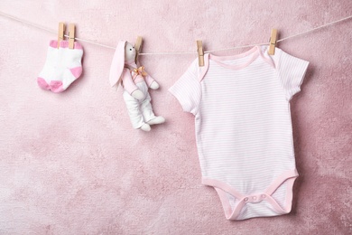 Photo of Baby clothes and toy hanging on rope near color wall. Space for text