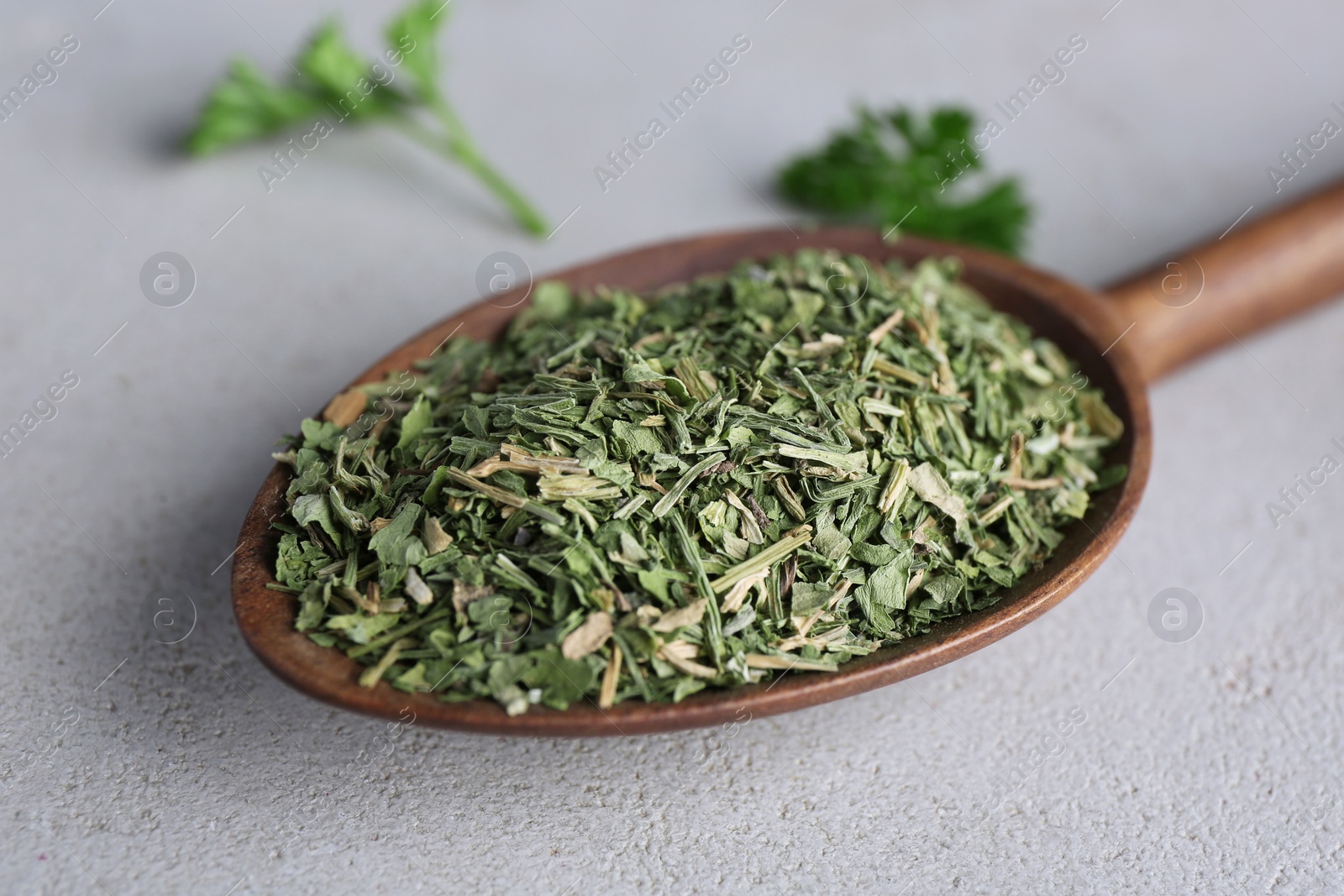 Photo of Spoon with dry parsley on grey table