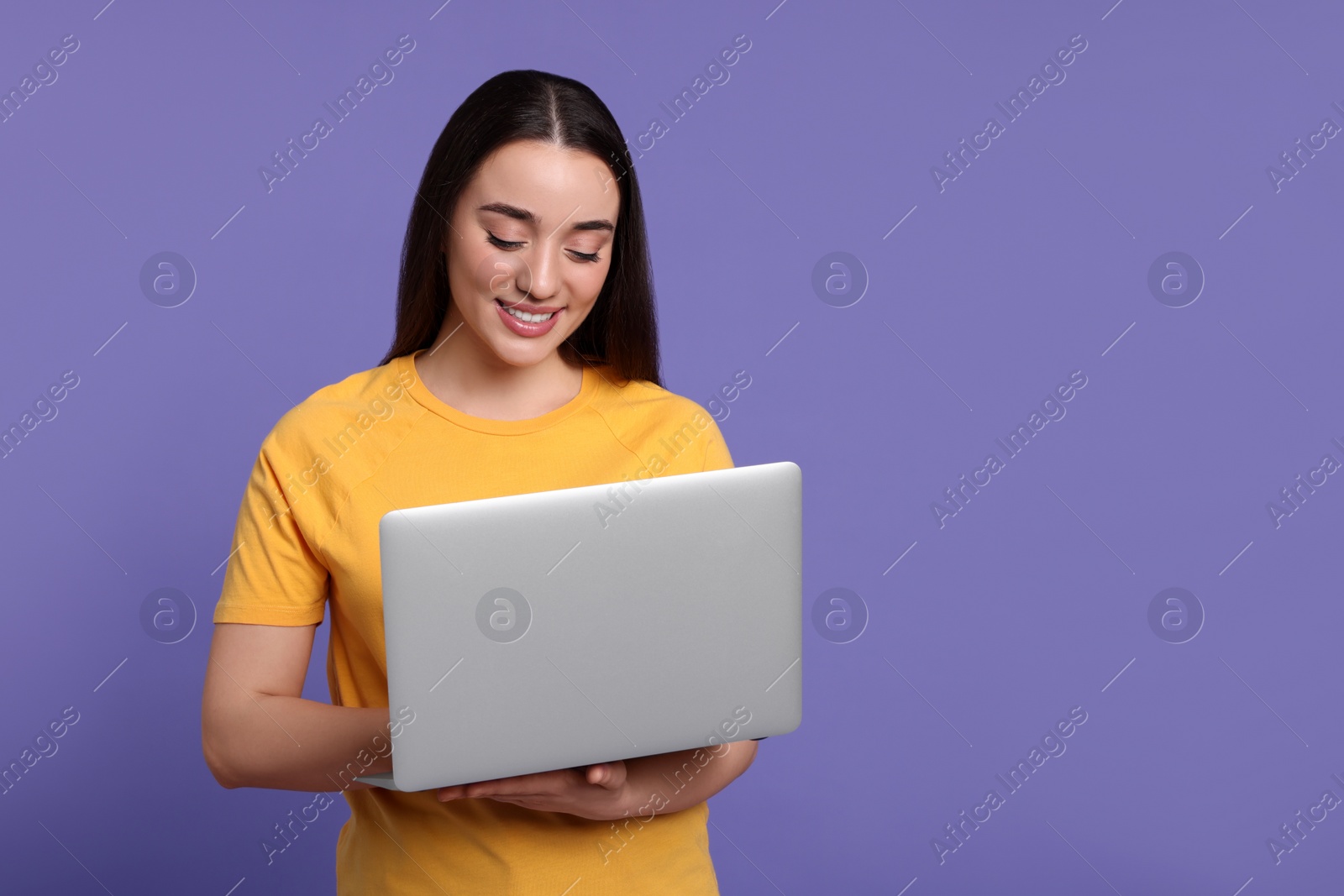 Photo of Smiling young woman working with laptop on lilac background, space for text