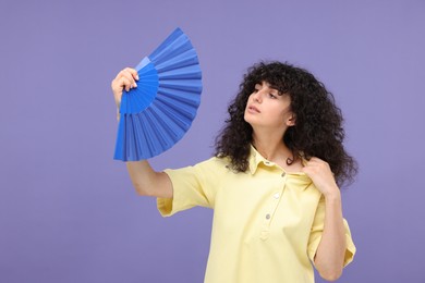 Photo of Woman with hand fan suffering from heat on purple background