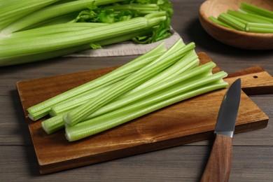Photo of Board with fresh green celery and knife on wooden table