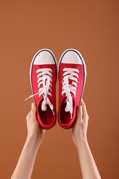 Photo of Woman with red classic old school sneakers on brown background, closeup