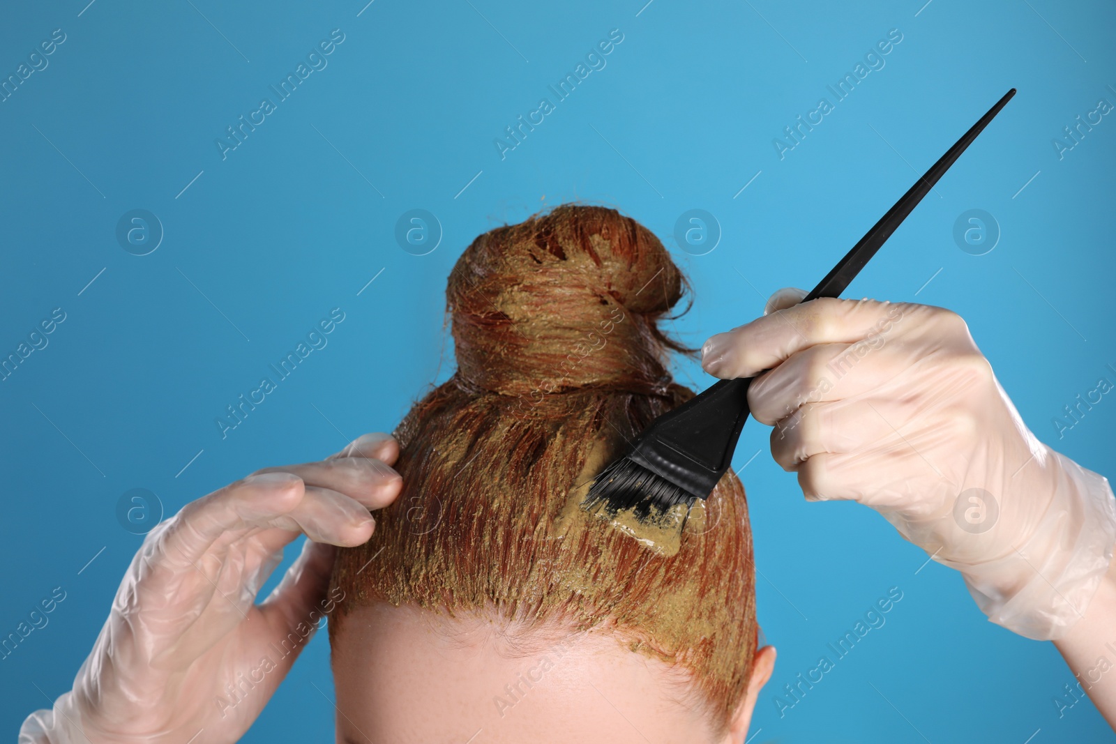 Photo of Young woman dyeing her hair with henna on light blue background, closeup