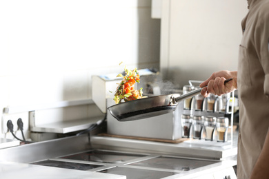 Male chef cooking tasty food on stove in restaurant 
kitchen, closeup of hand