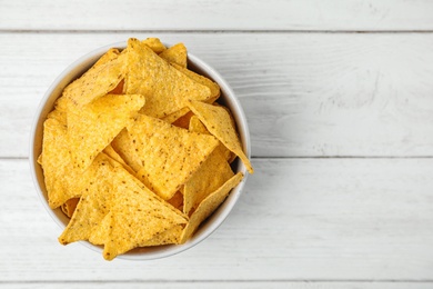 Photo of Bowl with tasty Mexican nachos chips on white wooden table, top view. Space for text