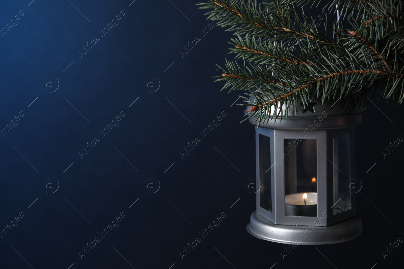 Photo of Christmas lantern with burning candle on fir tree against blue background, closeup. Space for text