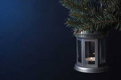 Photo of Christmas lantern with burning candle on fir tree against blue background, closeup. Space for text