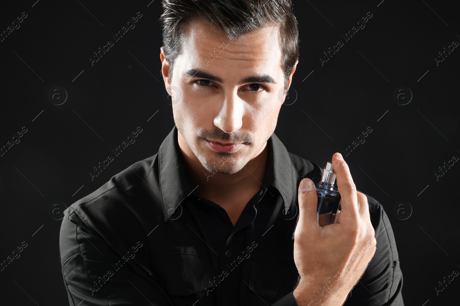 Photo of Handsome young man using perfume on black background