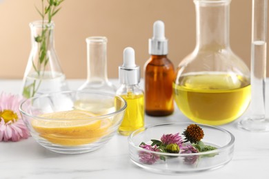 Photo of Developing cosmetic oil. Laboratory glassware, lemon and flowers on white table