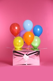 Gift box with bright air balloons on color background