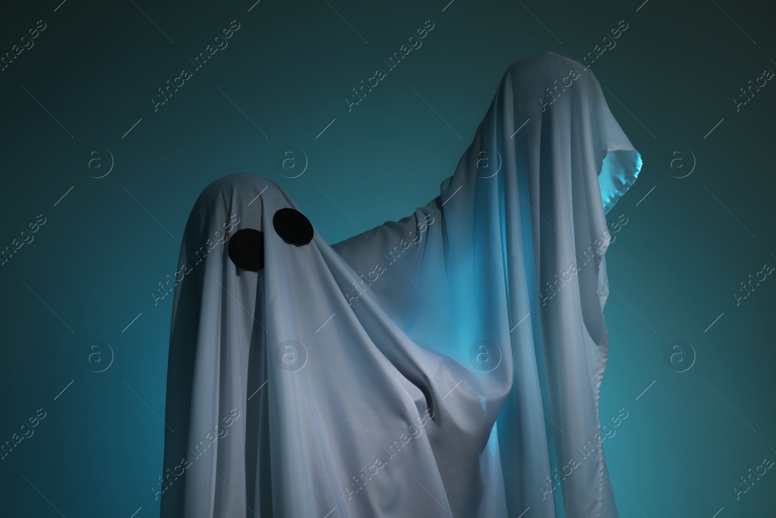 Photo of Creepy ghost. Woman covered with sheet on dark teal background