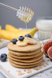Photo of Pouring honey onto tasty oatmeal pancakes, closeup
