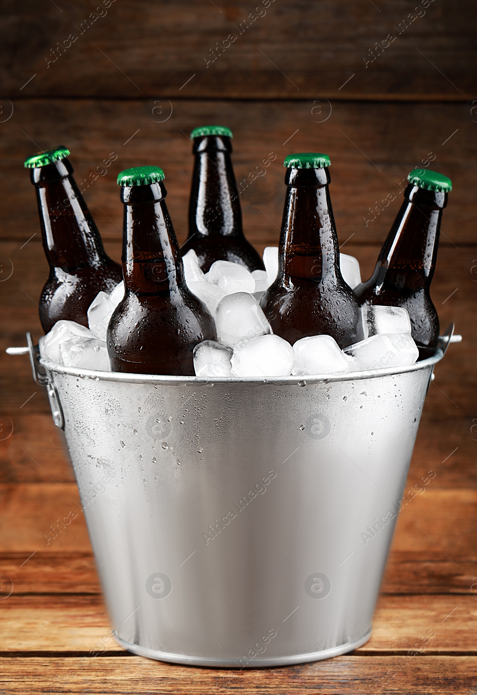 Photo of Metal bucket with bottles of beer and ice cubes on wooden table