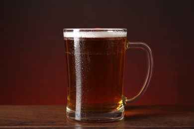 Photo of Mug with fresh beer on wooden table against color background