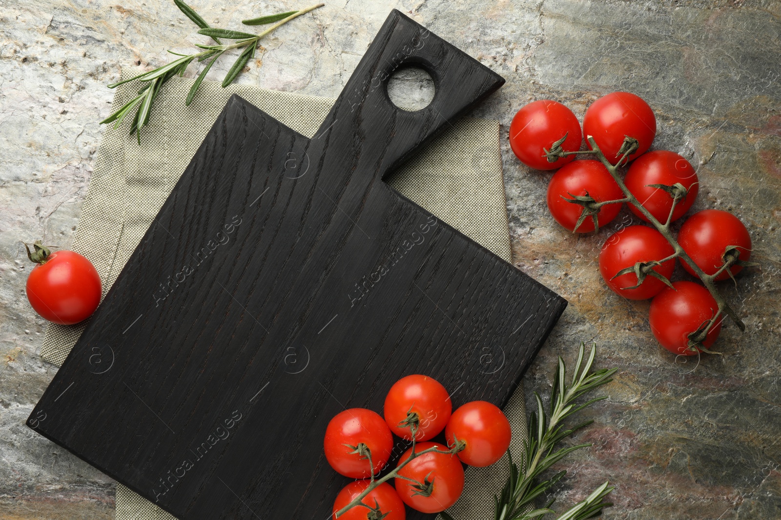 Photo of Black cutting board, tomatoes and rosemary on textured table, flat lay