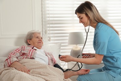 Photo of Young caregiver measuring blood pressure of senior woman in room. Home health care service