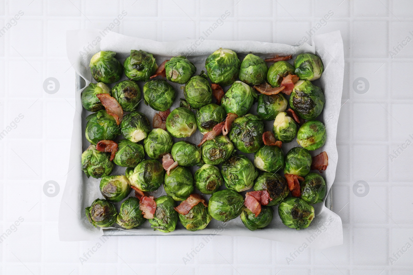 Photo of Delicious roasted Brussels sprouts and bacon in baking dish on white tiled table, top view