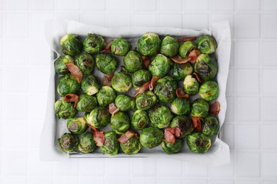 Delicious roasted Brussels sprouts and bacon in baking dish on white tiled table, top view